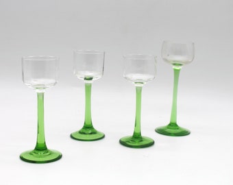 May include: Four clear glass cordial glasses with green stems and bases. The glasses have a simple, elegant design, with a rounded bowl and a slender stem. The green colour adds a pop of colour to the otherwise transparent glasses.