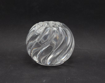 May include: Clear glass votive candle holder with a spiral design. The round holder has a wide opening and is made of transparent glass. The swirling pattern creates a textured effect, reflecting light. The candle holder is suitable for home decor.