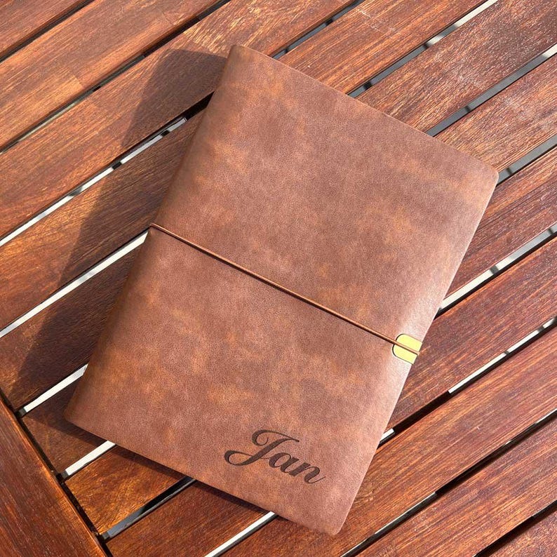 May include: A brown leather-bound journal with a gold clasp and the name "Jan" engraved on the front.