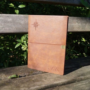 May include: A brown leather journal with a compass design and the initials "A. &." embossed on the cover.