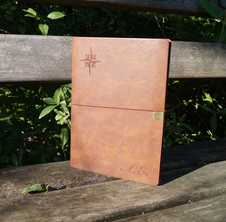 May include: A brown leather journal with a compass design and the initials "A. &." embossed on the cover.