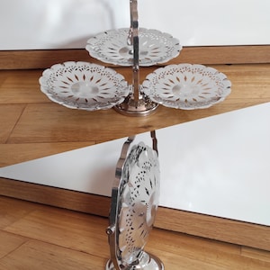 Könnte beinhalten: Ein dreistöckiger Servierständer aus Silber mit einem Griff. Jede Etage hat ein dekoratives, durchbrochenes Design.