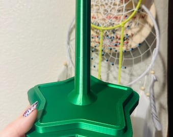 Peut inclure: Un présentoir vert vif en forme d'étoile avec un poteau central. Le support a un design en couches et est tenu par une main. L'arrière-plan comprend un attrape-rêves.