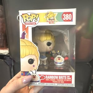 May include: A Funko Pop Animation vinyl figure set featuring Rainbow Brite and Twink, numbered 380. The box displays the characters with blonde hair, a blue outfit, and a white creature with red gloves. The packaging includes the text Rainbow Brite.