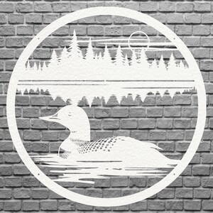 May include: White metal wall art featuring a loon swimming on a lake, with a forest and sun in the background. The design is circular and set against a gray brick wall. The loon has detailed feather patterns.