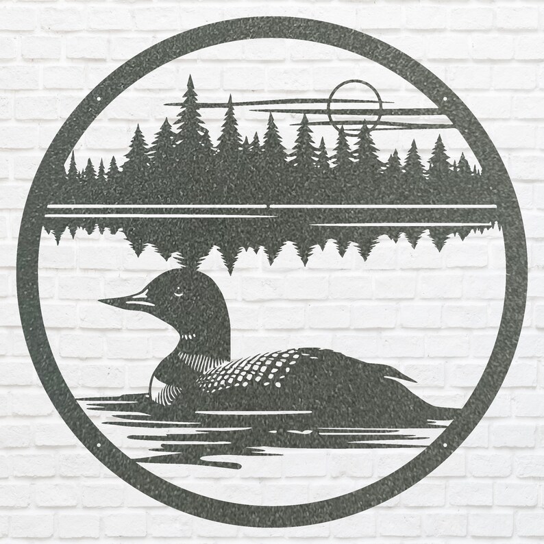 May include: A circular metal wall art piece depicting a loon swimming on a lake with a forest and moon in the background. The artwork is in a dark gray color and is mounted on a white brick wall.