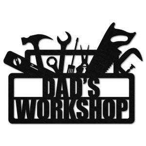 May include: Black metal sign with the text "Dad's Workshop" and a silhouette of a toolbox with various tools, including a hammer, wrench, saw, and screwdriver.