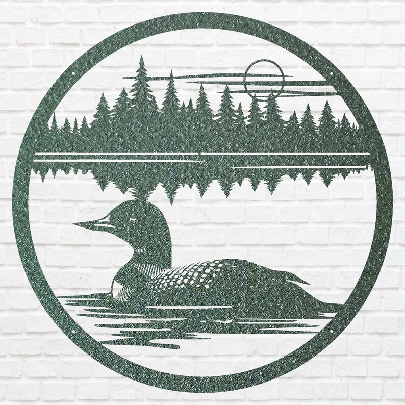 May include: A circular metal wall art piece featuring a loon swimming on a lake, with a forest and sun in the background. The artwork is a dark green color and is set against a white brick wall.