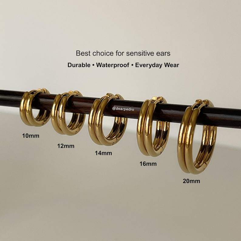 Gold hinged hoop earrings in 316L surgical steel displayed on a horizontal rod, showing size comparison from 10mm to 20mm with labeled sizes 10mm, 12mm, 14mm, 16mm, and 20mm
