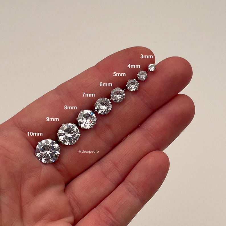 Close-up of cubic zirconia stud earrings in sizes 3mm to 10mm displayed on fingers, showcasing their brilliant diamond-like sparkle, crafted with hypoallergenic 316L surgical steel for sensitive ears