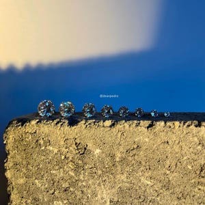 Lineup of cubic zirconia stud earrings in sizes 3mm to 10mm, glowing brilliantly in natural light, crafted with durable 316L surgical steel, hypoallergenic and perfect for sensitive ears