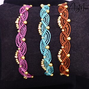 May include: Three braided bracelets with gold beads. The bracelets are pink, teal, and brown.