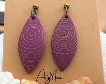 Könnte beinhalten: Ein Paar violette und goldene, blattartige Ohrringe mit einem Spiralmuster. Die Ohrringe hängen an einer braunen Karte mit dem Text "Arty Misa."