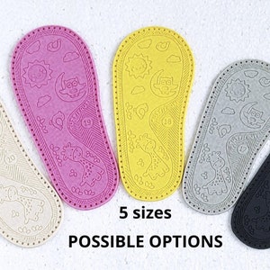 May include: Five pairs of baby shoe soles in different colours: beige, pink, yellow, grey, and black. Each sole has a unique design featuring a sun, moon, owl, and giraffe. The text "5 sizes" and "POSSIBLE OPTIONS" is printed below the soles.