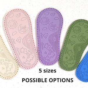May include: Five pairs of baby shoe soles in different colours: beige, pink, purple, green, and blue. Each sole has a design of a sun, moon, owl, and giraffe. The text "5 sizes" and "POSSIBLE OPTIONS" is printed below the soles.