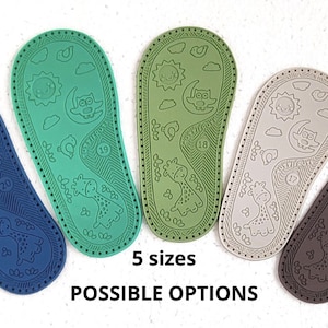 May include: Five pairs of baby shoe soles in different colours: blue, green, beige, and brown. Each sole has a pattern of a sun, moon, owl, and giraffe. The text "5 sizes" and "POSSIBLE OPTIONS" is printed below the soles.