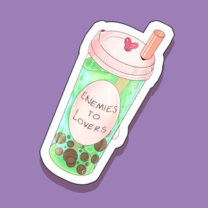 May include: A sticker of a green bubble tea with a white lid and a straw. The text "Enemies to Lovers" is on the side of the cup.