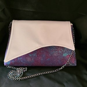 May include: A small, light pink and purple clutch purse with a silver chain strap. The purse has a flap that folds over the front and is secured with a magnetic closure.