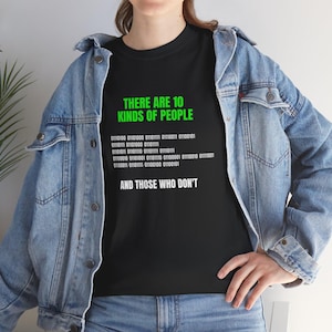 May include: Black t-shirt featuring the text "THERE ARE 10 KINDS OF PEOPLE" in green, binary code, and the phrase "AND THOSE WHO DON'T" in white. The shirt is paired with a blue denim jacket.