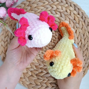Peut inclure: Deux axolotls crochetés à la main. L'un est rose et blanc avec des branchies rose vif, l'autre est jaune et orange. Les deux ont des yeux noirs. Les axolotls sont faits de fil doux et moelleux.