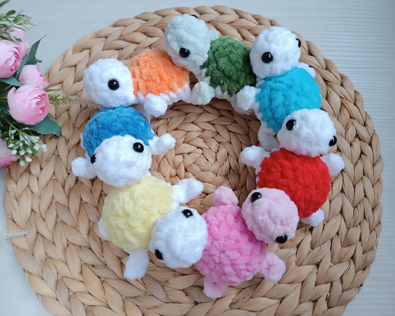 Pu&ograve; includere: Una collezione di giocattoli di tartaruga all'uncinetto in vari colori, tra cui blu, rosso, giallo, rosa, verde e arancione. Le tartarughe sono disposte in cerchio su un cesto intrecciato.