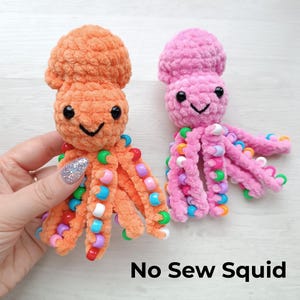Puede incluir: Dos juguetes de pulpo hechos a mano con ganchillo. Uno es naranja, el otro rosa. Cada uno tiene ojos negros y una boca sonriente. Los tentáculos están adornados con cuentas de colores. El texto "No Sew Squid" está en la parte inferior.