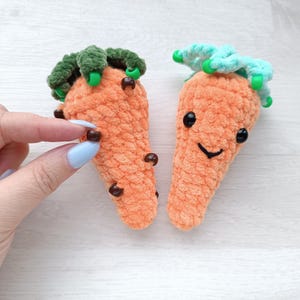May include: Two plush orange carrot-shaped toys with green and blue tops. One carrot has a smiling face with black eyes and a curved mouth. The other carrot has brown bead-like details. The toys are handmade.