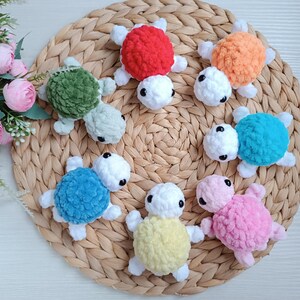 Pu&ograve; includere: Sette giocattoli di tartaruga all'uncinetto in vari colori, tra cui verde, rosso, arancione, blu, rosa e giallo. Le tartarughe sono disposte su un tappetino di paglia intrecciata.