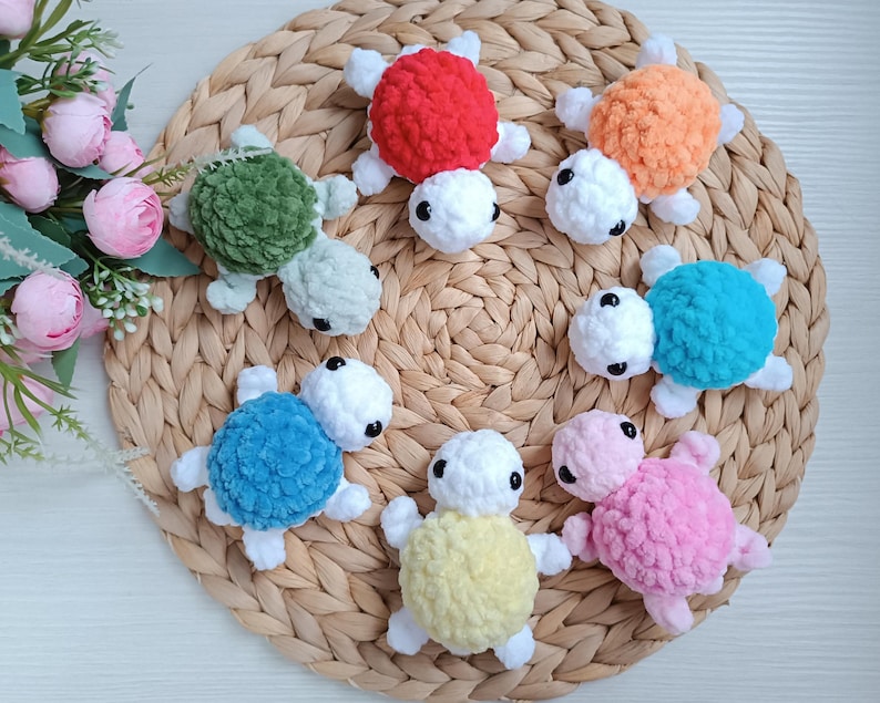 Pu&ograve; includere: Otto giocattoli di tartaruga all'uncinetto in vari colori, tra cui rosso, arancione, verde, blu, rosa e giallo. Le tartarughe sono disposte su una superficie di vimini intrecciato.