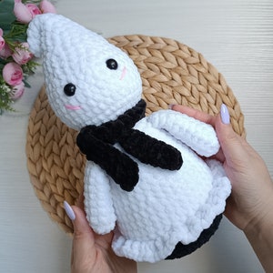 Könnte beinhalten: Weißes gehäkeltes Geister-Plüschtier mit einem schwarzen Samt-Schal. Der Geist hat ein lächelndes Gesicht mit schwarzen Augen und rosa Wangen.