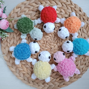 Pu&ograve; includere: Sette giocattoli di tartaruga all'uncinetto in diversi colori, tra cui rosso, arancione, verde, blu, giallo, rosa e bianco. Le tartarughe sono disposte in cerchio su una superficie di vimini intrecciato.