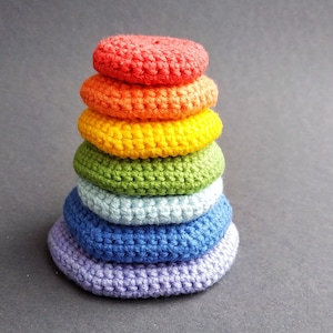 K&ouml;nnte beinhalten: Ein Stapel aus sechs geh&auml;kelten Ringen in Regenbogenfarben, beginnend mit Rot oben und endend mit Lila unten.