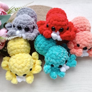 Puede incluir: Seis peluches de pulpo de crochet en diferentes colores, incluyendo gris, amarillo, turquesa, rojo y rosa. Los peluches tienen ojos blancos y una boca blanca.