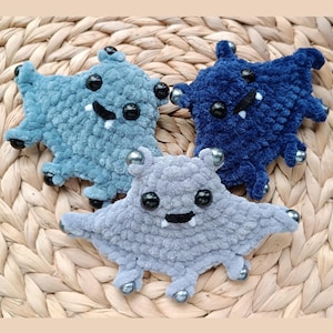 May include: Three handmade plush monster toys in shades of blue and gray. Each has a smiling face with black eyes and a small mouth. The toys have small arms and legs with silver ball accents. The toys are made of a soft, textured material.