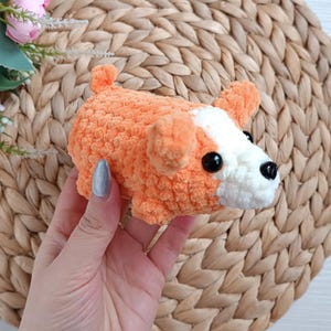 May include: A small crocheted orange and white dog plush toy. The toy has black eyes and a white nose.