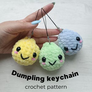 Puede incluir: Tres llaveros de peluche con forma de bola de masa en amarillo, verde claro y azul claro, cada uno con ojos de seguridad negros, una sonrisa negra bordada y mejillas rosadas. Cada llavero está unido a un cordón negro con un cierre de metal plateado.