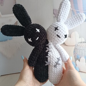 May include: Two crocheted plush bunny toys, one black and one white, with stitched-on eyes and a stitched-on line down the middle of their bodies, as if they are joined together.