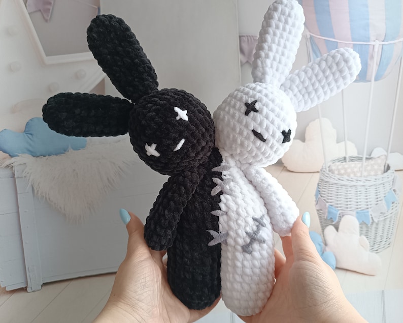May include: Two crocheted plush bunny toys, one black and one white, with stitched-on eyes and a stitched-on line down the middle of their bodies, as if they are joined together.
