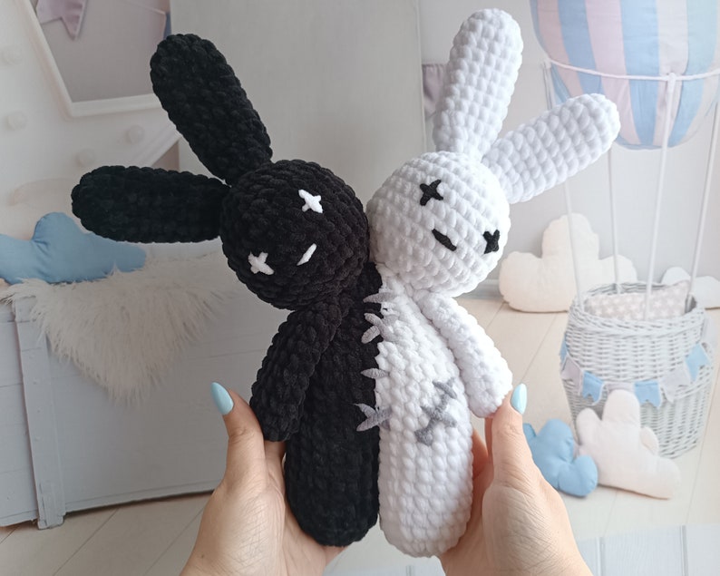 May include: Two crocheted bunny plushies, one black and one white, are sewn together at the seam. Both bunnies have black eyes and a stitched-on X for a mouth.
