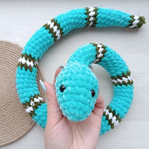 May include: A crocheted turquoise snake toy with white and green accents. The snake is curled up in a circle and has a plush texture.
