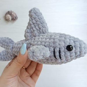 May include: A gray crocheted shark plush toy with black eyes and a stitched mouth.