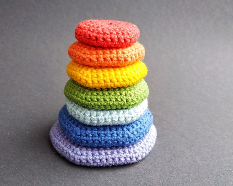 K&ouml;nnte beinhalten: Ein Stapel aus sechs geh&auml;kelten Ringen in Regenbogenfarben, beginnend mit Rot oben und endend mit Lila unten.
