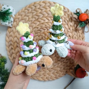 Puede incluir: Dos adornos de tortuga de árbol de Navidad hechos a mano con ganchillo. Las tortugas tienen caparazones verdes en forma de árbol con adornos de cuentas de colores y estrellas amarillas. Las tortugas tienen cuerpos verde claro y patas color canela.