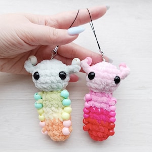May include: Two handmade crochet monster charms. One is light green with a rainbow beaded body, the other is pink with a red beaded body. Both have black eyes and small horns. Each charm has a black string attached.