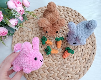 May include: A collection of handmade crochet bunnies in pink, brown, and gray, with black eyes and small carrot decorations. The bunnies are made of soft, textured yarn and are arranged on a woven mat.