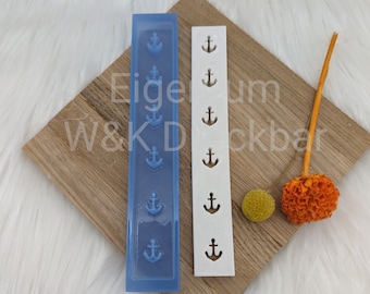 May include: A blue silicone mold and a white plastic mold, both with a design of multiple anchors. The molds are on a wooden surface. The text "Eigeum W&K Dckbar" is visible on the surface. The text "W&K Druckbar" is visible in the lower left corner.