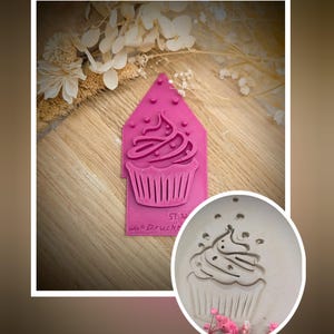 Könnte beinhalten: Ein rosa Stempel in Cupcake-Form mit einem detaillierten Cupcake-Design. Der Stempel hat einen Griff und den Text "St. M Wax Druckt". Ein kreisförmiger Abdruck des Stempels ist ebenfalls abgebildet.