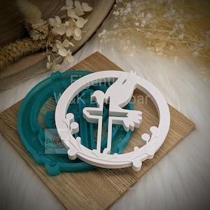 Könnte beinhalten: Weißes Tauben- und Kreuzdesign, möglicherweise eine Form oder Dekoration, auf einer Holzoberfläche. Das Design umfasst ein Kreuz, eine Taube und einen kreisförmigen Rahmen mit floralen Akzenten. Im Hintergrund ist eine türkisfarbene Form mit dem Text "W&K Druckbar" zu sehen.