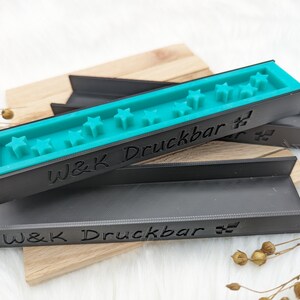 May include: Two black plastic moulds with the text "W&K Druckbar" on them. The top mould has a turquoise blue insert with a row of five star shapes.