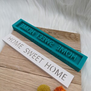 May include: Two rectangular signs with the text "Home Sweet Home" in raised letters. The top sign is teal and the bottom sign is white.